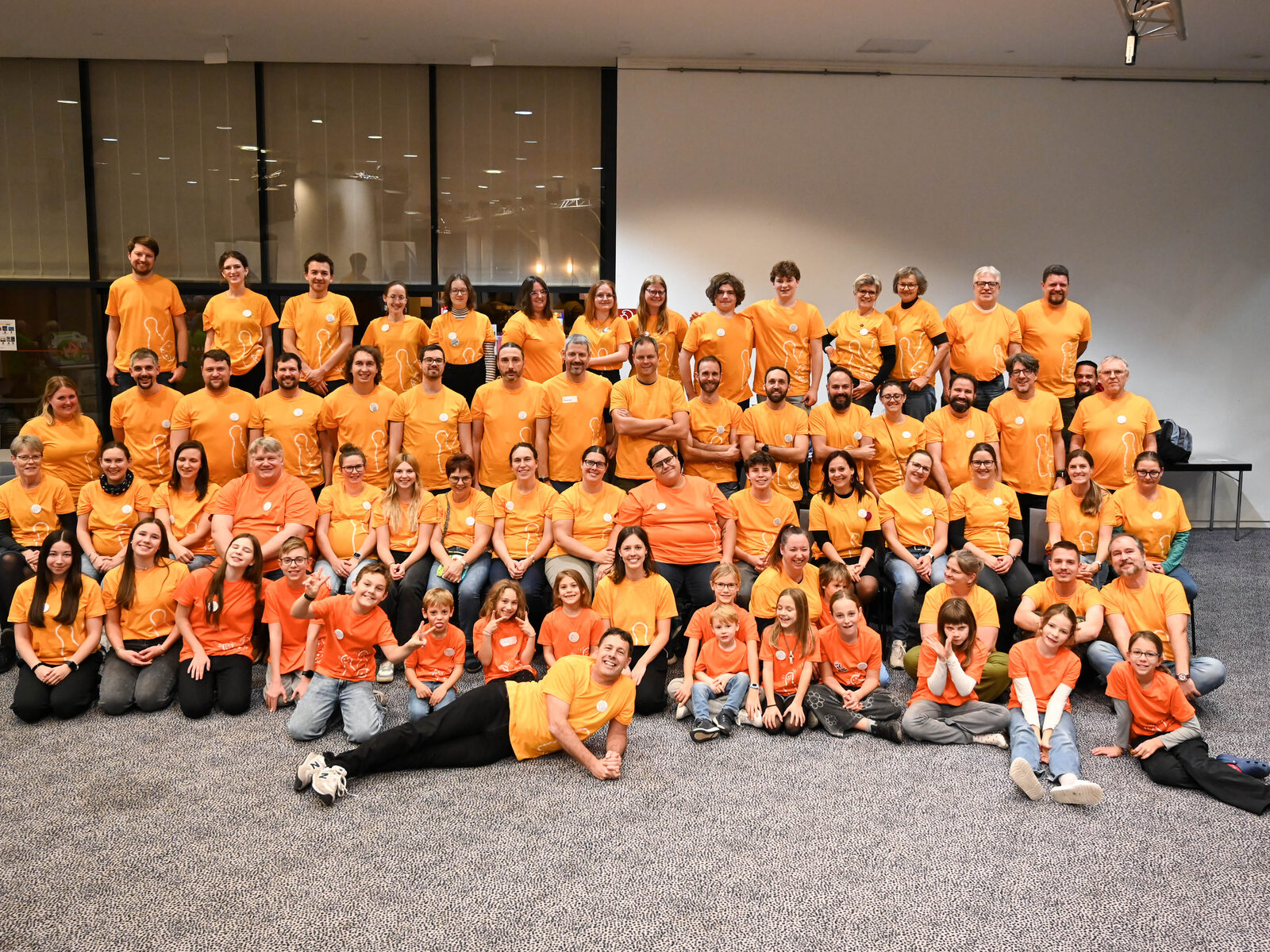 Gruppenfoto des Teams der Kärntner Spieletage: Erwachsene und Kinder in orangen Vereinsshirts, stehend, sitzend und vorne einer liegend
